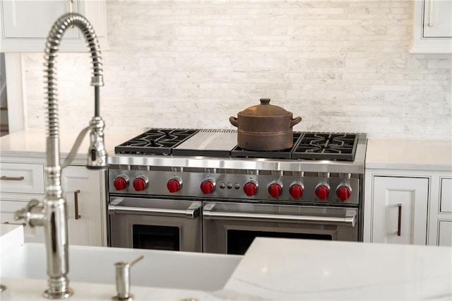 interior details with tasteful backsplash, white cabinetry, range with two ovens, and light countertops