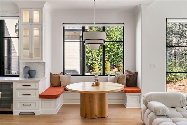 sitting room with beverage cooler, ornamental molding, and light wood-style flooring