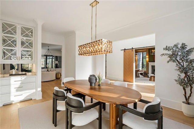 dining room with light wood finished floors, a barn door, baseboards, and crown molding