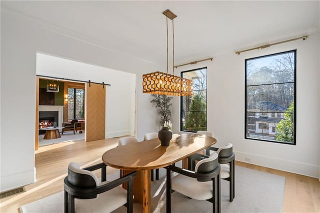 dining space with visible vents, a barn door, light wood-style floors, a lit fireplace, and baseboards