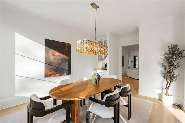 dining room featuring light wood-style floors, baseboards, a chandelier, and crown molding