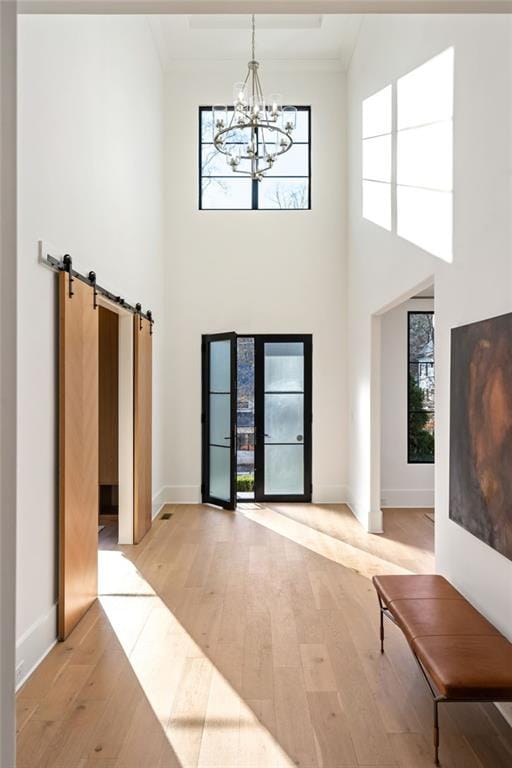 interior space with a notable chandelier, a high ceiling, baseboards, light wood-style floors, and ornamental molding