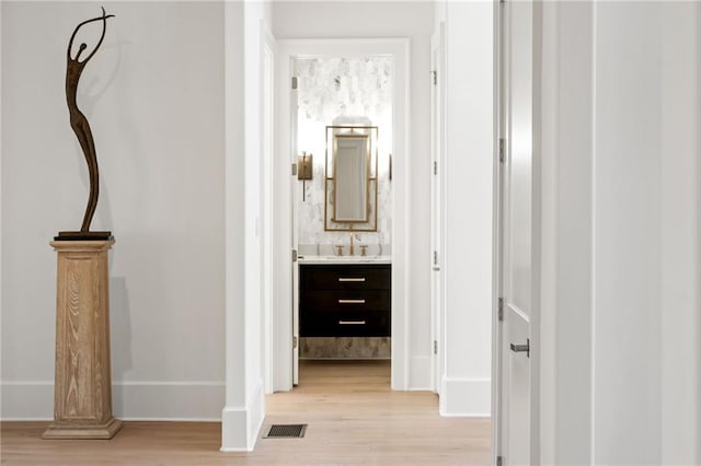 hallway featuring visible vents, a sink, light wood-style flooring, and baseboards