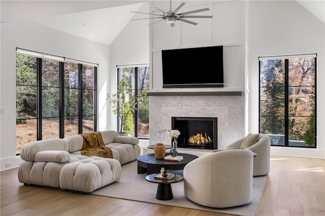 living room featuring ceiling fan, a lit fireplace, wood finished floors, and high vaulted ceiling