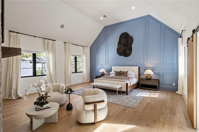 bedroom with lofted ceiling, a barn door, a decorative wall, and light wood-style flooring