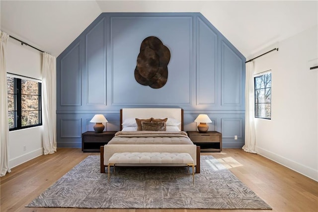 bedroom featuring lofted ceiling, light wood-style floors, and a decorative wall