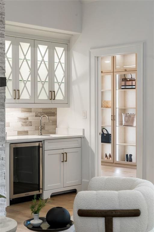 bar with wine cooler, tasteful backsplash, a sink, wood finished floors, and wet bar