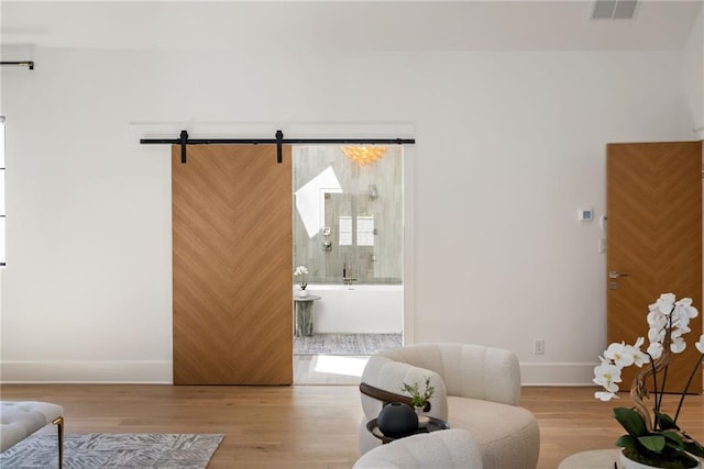 living area with a barn door, wood finished floors, visible vents, and baseboards