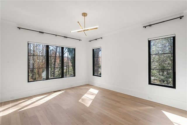 unfurnished room featuring visible vents, light wood-type flooring, a wealth of natural light, and baseboards