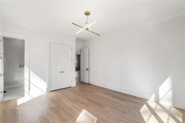 unfurnished bedroom with ensuite bath, light wood-style flooring, baseboards, and a closet