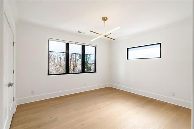 empty room with light wood-style floors, visible vents, ornamental molding, and baseboards