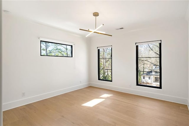 unfurnished room featuring a notable chandelier, light wood finished floors, a wealth of natural light, and baseboards