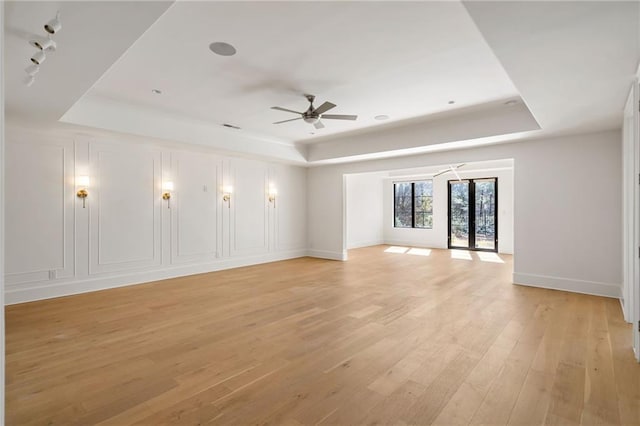 spare room with a ceiling fan, a tray ceiling, and light wood-style flooring