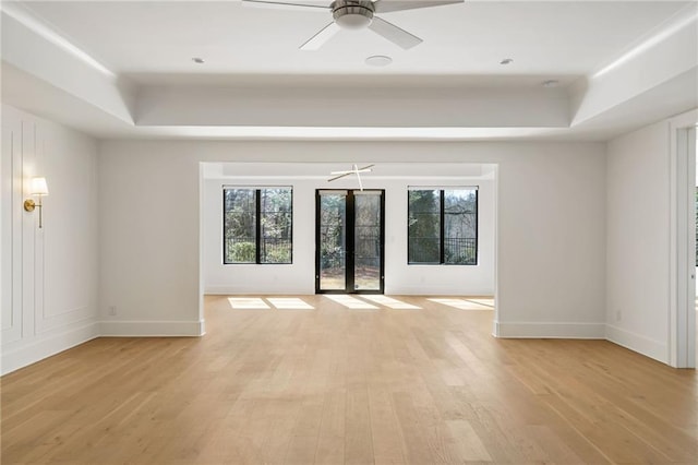 spare room with french doors, light wood-type flooring, a raised ceiling, and baseboards