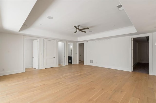 unfurnished bedroom featuring a tray ceiling, visible vents, light wood-style flooring, and baseboards