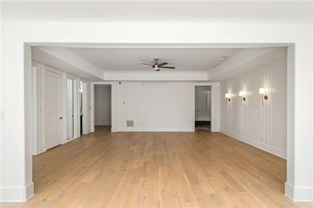 unfurnished living room featuring baseboards, visible vents, a raised ceiling, a ceiling fan, and light wood-style floors