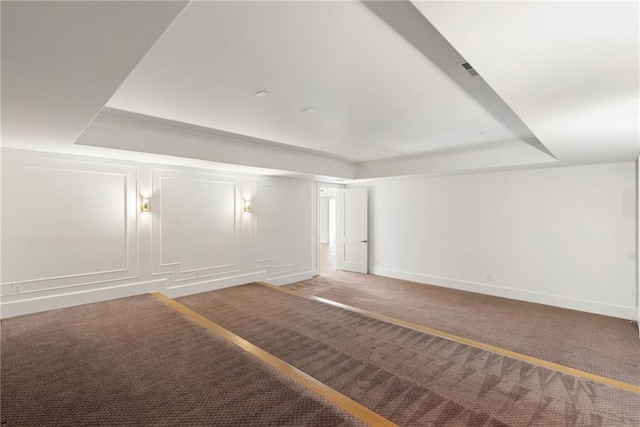 unfurnished room with a tray ceiling, baseboards, a decorative wall, and carpet