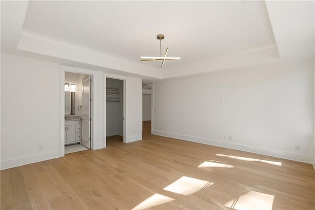 unfurnished bedroom with light wood-style floors, baseboards, and a tray ceiling