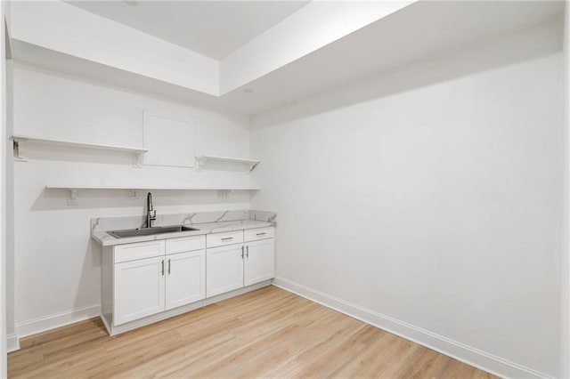 kitchen with light wood finished floors, open shelves, light countertops, a sink, and baseboards