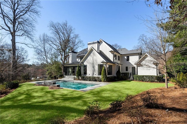 back of property with a chimney, a lawn, board and batten siding, a sunroom, and an outdoor pool