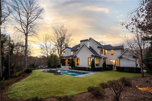 back of property with an outdoor pool and a lawn