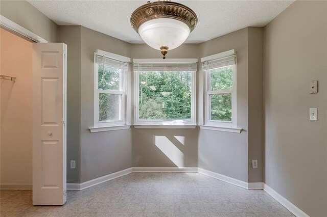unfurnished room with a textured ceiling, baseboards, and a healthy amount of sunlight