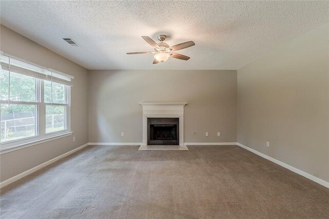 unfurnished living room with a textured ceiling, carpet, a ceiling fan, a fireplace with flush hearth, and visible vents