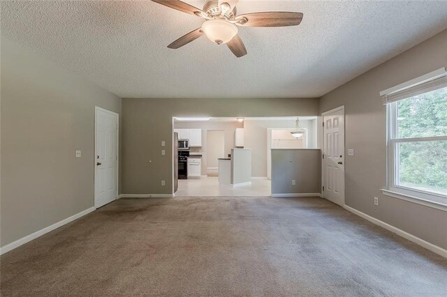 unfurnished living room featuring a ceiling fan, a textured ceiling, and light carpet