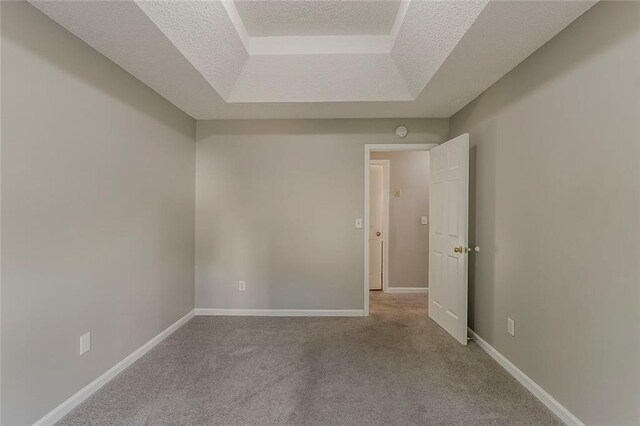 unfurnished room with a raised ceiling, carpet floors, baseboards, and a textured ceiling