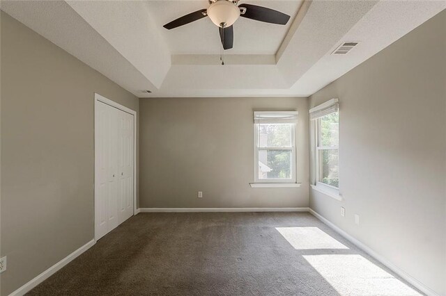 carpeted empty room with baseboards, ceiling fan, a tray ceiling, and visible vents