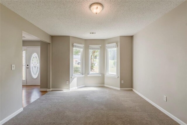 interior space featuring baseboards, carpet flooring, a textured ceiling, and visible vents