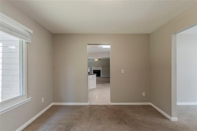 spare room featuring light colored carpet, a textured ceiling, baseboards, and a fireplace