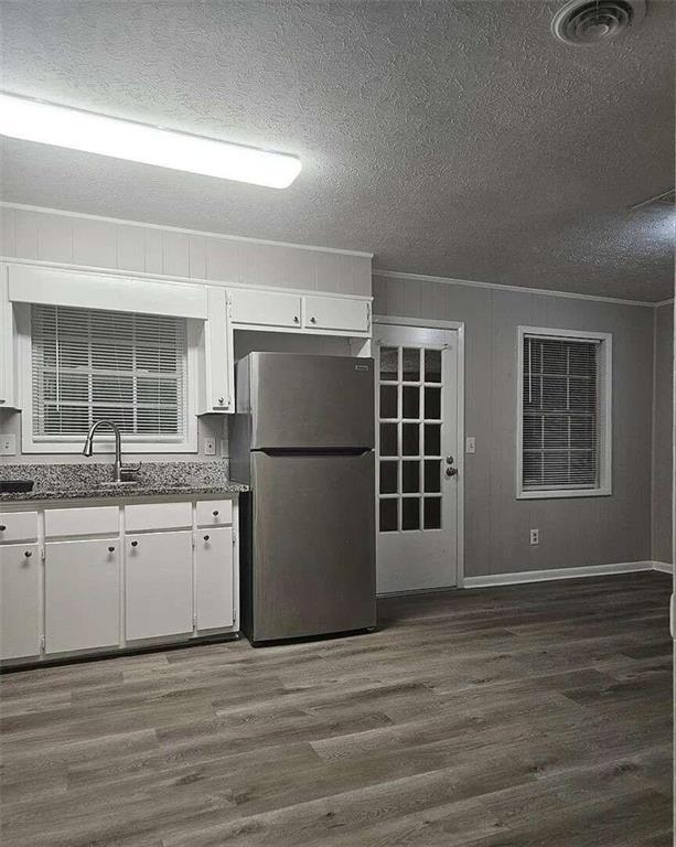 kitchen with a textured ceiling, stainless steel fridge, dark wood-type flooring, and white cabinetry