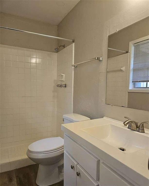 bathroom with wood-type flooring, tiled shower, vanity, and toilet