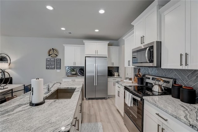 kitchen with white cabinetry, sink, stainless steel appliances, light stone countertops, and light hardwood / wood-style flooring