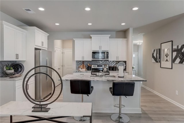 kitchen featuring stainless steel appliances, white cabinetry, an island with sink, and light stone counters