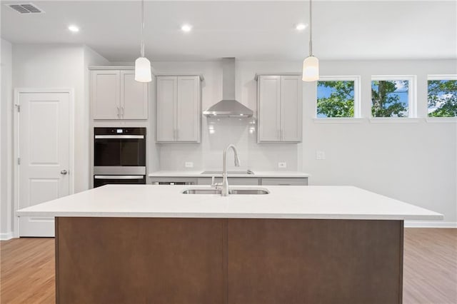 kitchen with light countertops, visible vents, wall chimney range hood, and light wood finished floors