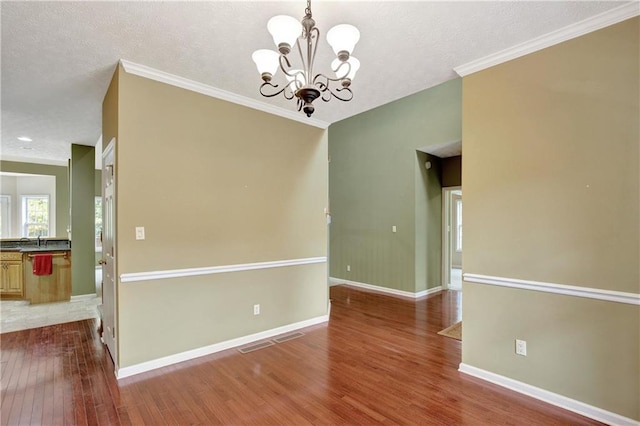 unfurnished room with wood-type flooring, a textured ceiling, ornamental molding, and a notable chandelier