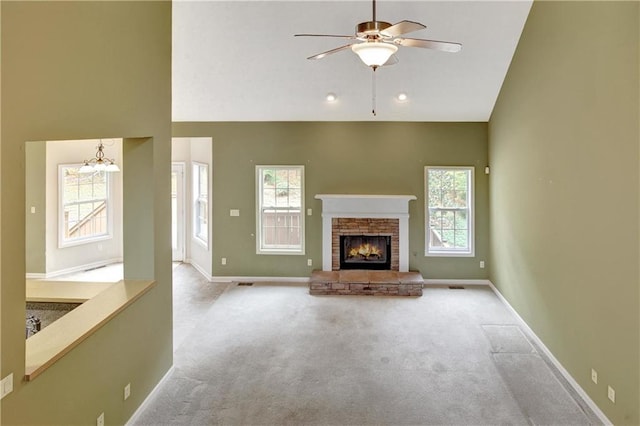 unfurnished living room with ceiling fan with notable chandelier, light colored carpet, a stone fireplace, and high vaulted ceiling