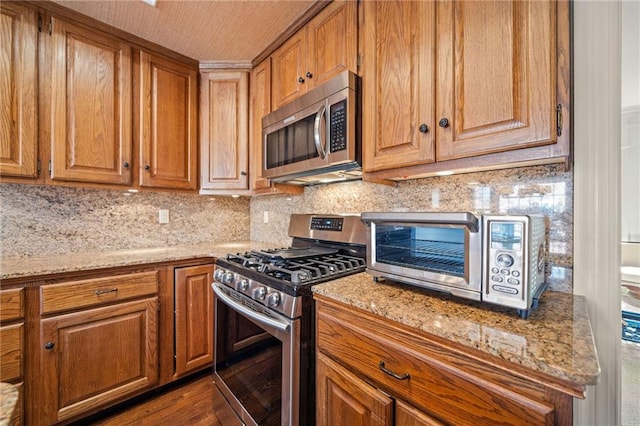 kitchen featuring stainless steel appliances, light stone countertops, dark hardwood / wood-style floors, and decorative backsplash