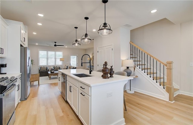 kitchen featuring sink, pendant lighting, stainless steel appliances, a kitchen island with sink, and white cabinets