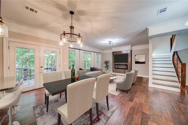 dining room with french doors, dark hardwood / wood-style flooring, a notable chandelier, a fireplace, and ornamental molding