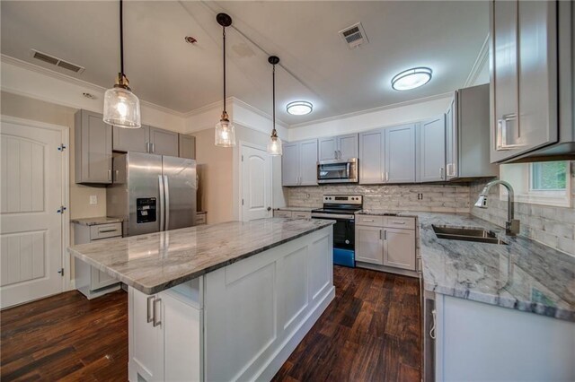 kitchen featuring appliances with stainless steel finishes, sink, decorative light fixtures, a center island, and dark hardwood / wood-style floors