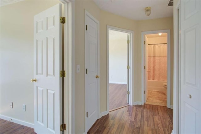 corridor featuring visible vents, baseboards, and dark wood-style flooring