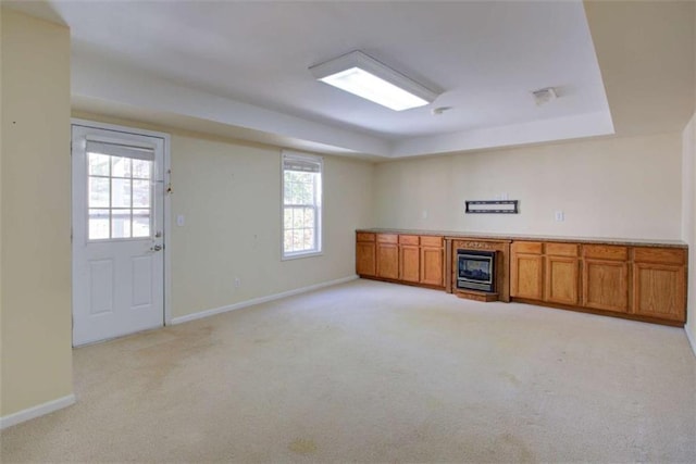 interior space with brown cabinetry, baseboards, a tray ceiling, a fireplace, and light carpet