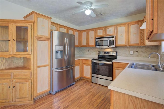 kitchen featuring a ceiling fan, light wood-type flooring, a sink, stainless steel appliances, and tasteful backsplash