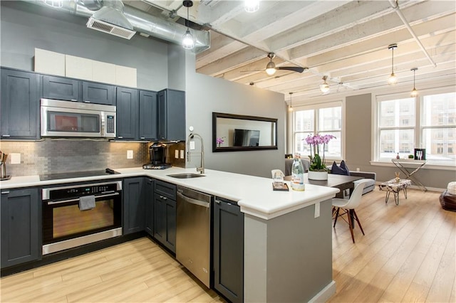 kitchen with light wood finished floors, stainless steel appliances, visible vents, a sink, and a peninsula