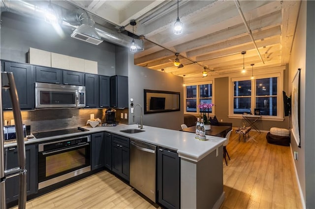 kitchen featuring stainless steel appliances, light wood-type flooring, a peninsula, and a sink