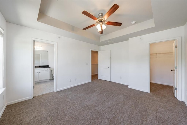 8475 Douglass Trl, Jonesboro, GA 30236 - unfurnished bedroom with a closet, baseboards, a tray ceiling, a walk in closet, and light carpet