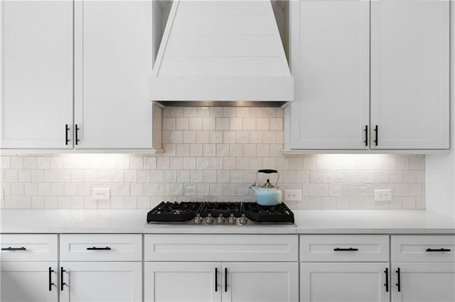 kitchen with premium range hood, stainless steel gas cooktop, light countertops, white cabinets, and backsplash